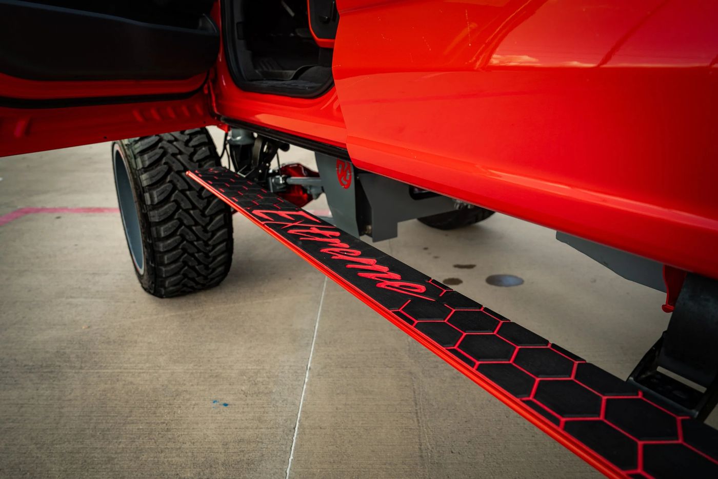 Close detail of a red lifted truck with a custom hex pattern rock step